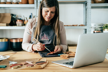Smiling Business Woman In Apron Using Her Laptop Computer For E-Learning While Painting Christmas...
