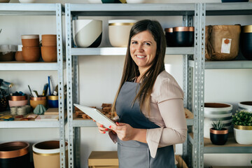 Sustainable Business: Portrait Of Smiling Business Woman In Apron Using Digital Tablet At Her Workshop 