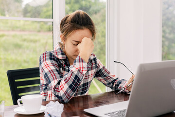 Woman stressed about work at home office and look at something on the laptop screen, The stress gave her a huge headache.