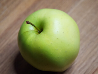 One apple of Golden cultivar on a wooden surface. Close-up shot.