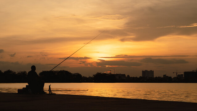 Silhouette of Asian man fishing in the river lake during sunset.
