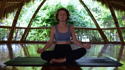 A beautiful woman meditates on a bamboo terrace in Asia. Meditation in the lotus position. A woman...