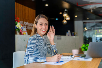 Attractive Asian Young woman freelancer working at the office using a laptop computer Looking at the camera at her comfortable workplace.