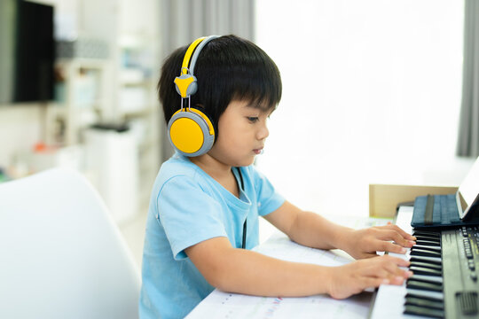 Cute asian toddler boy is trying to practice to play keyboard or piano in the living room at home, concept of learning, art, steam, musical, mental health, homeschool, skill, ability concept.