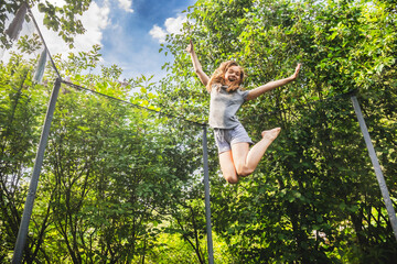 Preteen girl having fun bouncing on a trampoline in a backyard on a summer day