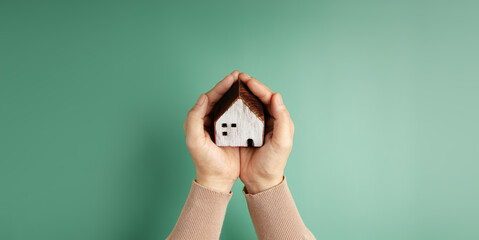 House and Family Insurance Concepts. Hand Holding a Wooden Toy House with Love and Gentle Care....