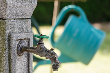  a water faucet in a graveyard with a blurred green watering can in the background © Uwe