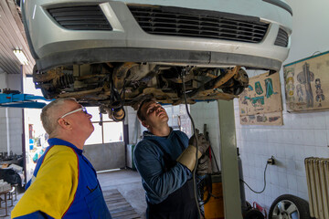 Manager controling welder who is working under the car