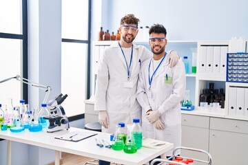 Young couple wearing scientist uniform hugging each other at laboratory