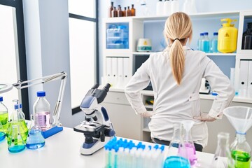 Middle age blonde woman working at scientist laboratory standing backwards looking away with arms...