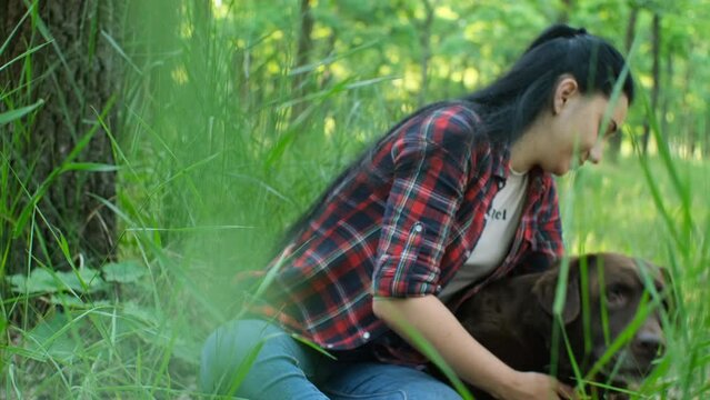  young caucasian woman in a red plaid shirt plays with an old labrador dog in a green park