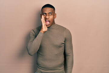 Young black man wearing casual turtleneck sweater shouting and screaming loud to side with hand on mouth. communication concept.