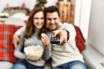 Young hispanic couple watching movie and eating popcorn sitting on the sofa at home.
