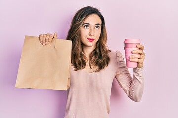 Young hispanic girl holding take away paper bag and coffee smiling looking to the side and staring...