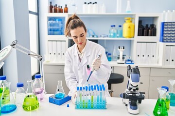 Young woman wearing scientist uniform using pipette working at laboratory