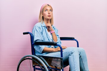 Beautiful blonde woman sitting on wheelchair thinking concentrated about doubt with finger on chin...