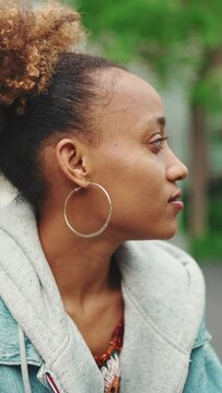 VERTICAL VIDEO: Close-up of nice young African American woman with ponytail in denim jacket enjoying morning coffee and looking away. Slow motion