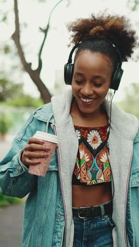 VERTICAL VIDEO: Smiling African Girl With Ponytail Wearing Denim Jacket, In Crop Top With National Pattern Walking Down The Street Listening To Music On Headphones And Dancing. Slow Motion 