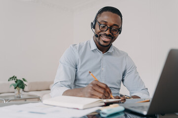 African american man in headset learns online at laptop, takes notes. Elearning, distance education