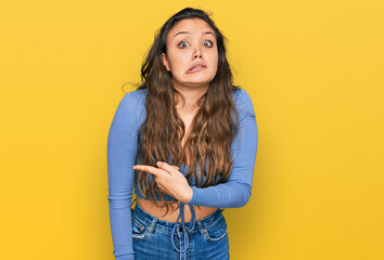 Young hispanic girl wearing casual clothes pointing aside worried and nervous with forefinger, concerned and surprised expression