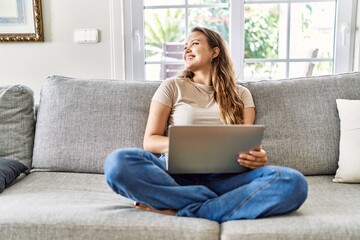 Obraz premium Young hispanic girl using laptop sitting on the sofa at home.