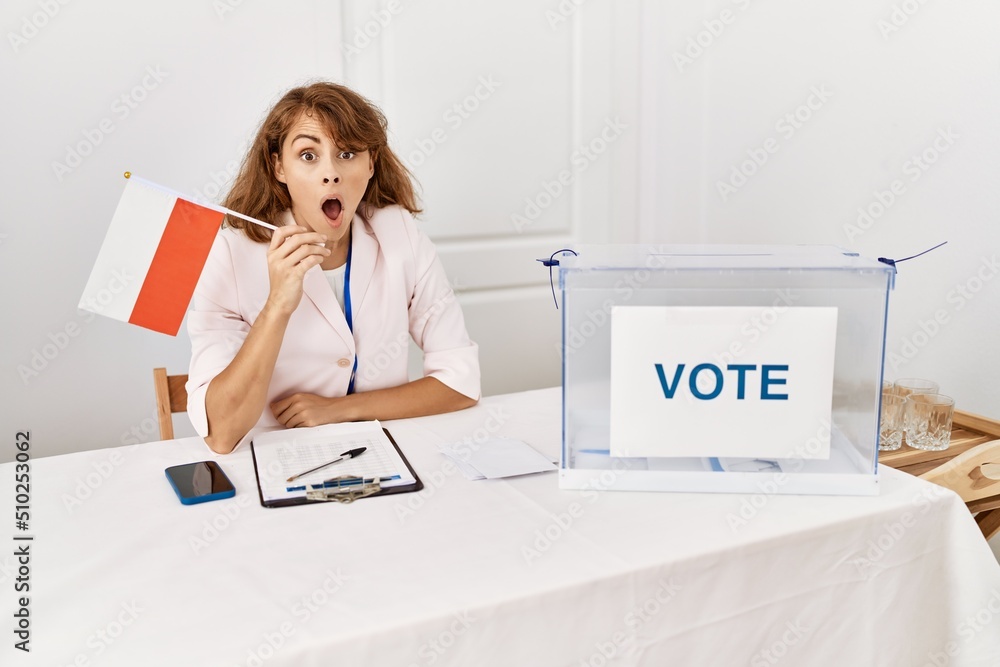 Canvas Prints Beautiful caucasian woman at political campaign election holding poland flag scared and amazed with open mouth for surprise, disbelief face