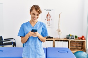Young caucasian physio therapist girl smiling happy using smartphone at the clinic.