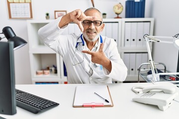 Obraz premium Mature doctor man at the clinic smiling making frame with hands and fingers with happy face. creativity and photography concept.