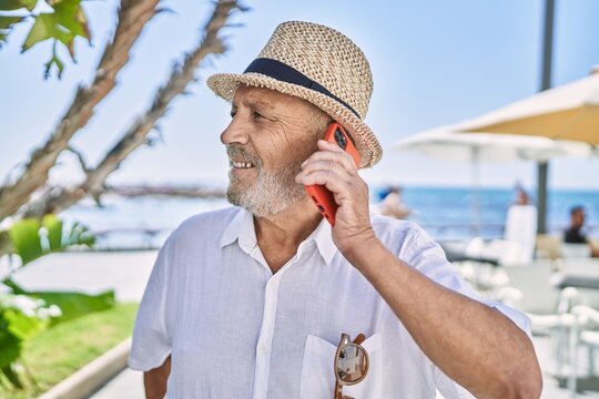 Senior man wearing summer hat talking on the smartphone at seaside
