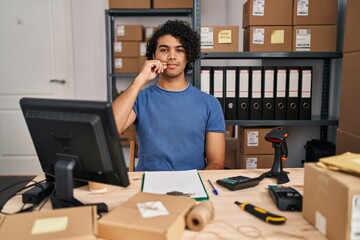 Hispanic man with curly hair working at small business ecommerce mouth and lips shut as zip with fingers. secret and silent, taboo talking