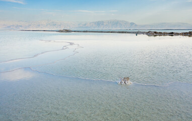 Israeli coast of the Dead Sea. salt mushroom  crystals formations, clear cyan green calm water near, typical landscape at Ein Bokek beach, Israel