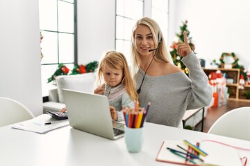Mother of caucasian daughter wearing call center agent headset at home surprised with an idea or question pointing finger with happy face, number one