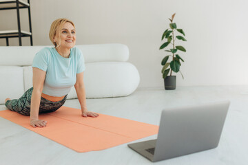 Portrait of happy senior woman doing fitness stretching exercises at home using laptop. Online training