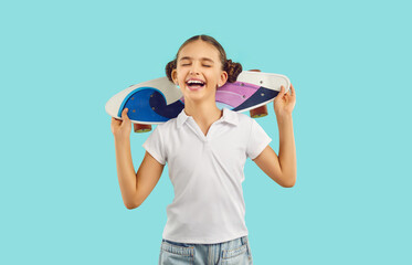 Studio shot of cheerful little kid with penny board. Happy pretty girl in white polo shirt standing...