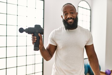 Young african american man smiling confident holding physiotherapy percussion gun at sport center