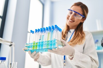 Young blonde woman wearing scientist uniform holding test tubes at laboratory