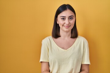 Hispanic girl wearing casual t shirt over yellow background with hands together and crossed fingers smiling relaxed and cheerful. success and optimistic