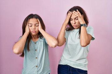 Young mother and daughter standing over pink background suffering from headache desperate and stressed because pain and migraine. hands on head.