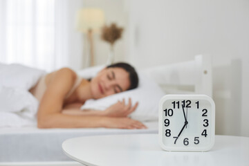 Close up of white plastic alarm clock set for 7 AM on bedside table in bedroom, with happy peaceful...