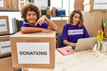 Young mother with little son wearing volunteer t shirt at donations stand smiling happy pointing with hand and finger