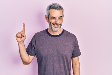 Handsome middle age man with grey hair pointing with index finger winking looking at the camera...