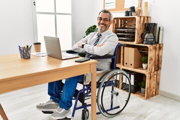 Middle age hispanic man working at the office sitting on wheelchair happy face smiling with crossed arms looking at the camera. positive person.