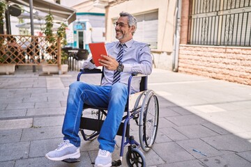 Middle age hispanic man sitting on wheelchair using touchpad at street