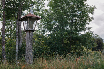 Wooden carved chapel pillar with trumpet angel on top near the way to the forest.