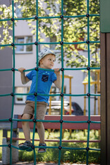Obraz premium Portrait of cute smiling boy climbing up the rope net he look at camera.