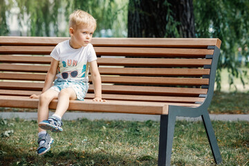Little boy sitting on a bench. baby alone in the city.