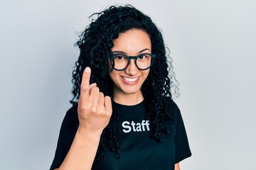 Young hispanic woman with curly hair wearing staff t shirt beckoning come here gesture with hand...