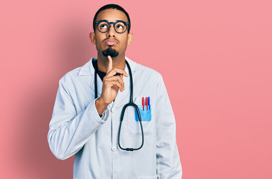 Young african american man wearing doctor uniform and stethoscope thinking concentrated about doubt with finger on chin and looking up wondering