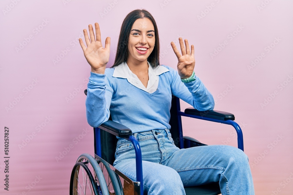 Wall mural Beautiful woman with blue eyes sitting on wheelchair showing and pointing up with fingers number nine while smiling confident and happy.