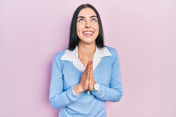 Beautiful woman with blue eyes standing over pink background begging and praying with hands together with hope expression on face very emotional and worried. begging.